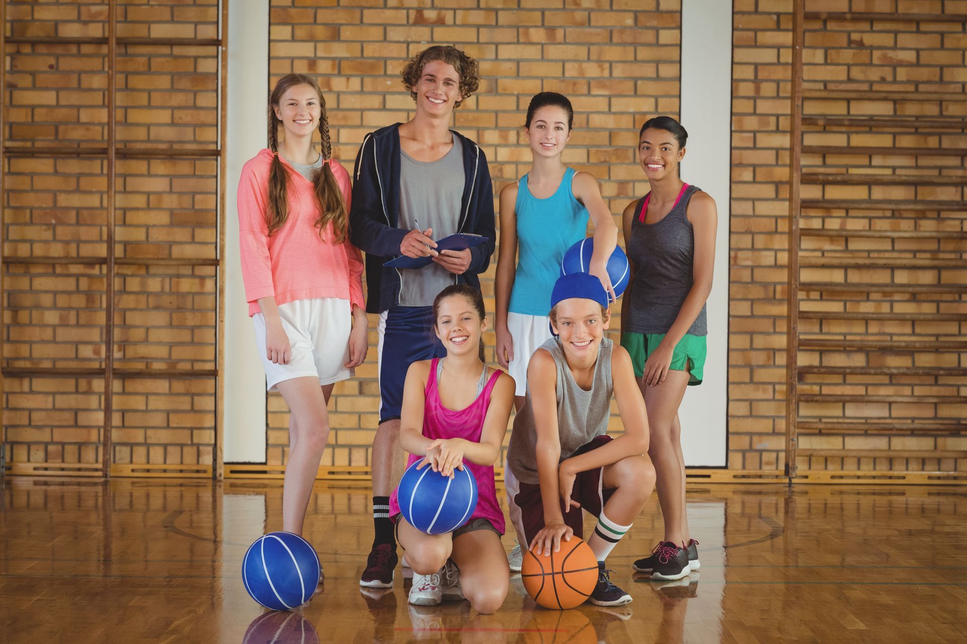 Group of teens in gym with basketballs.