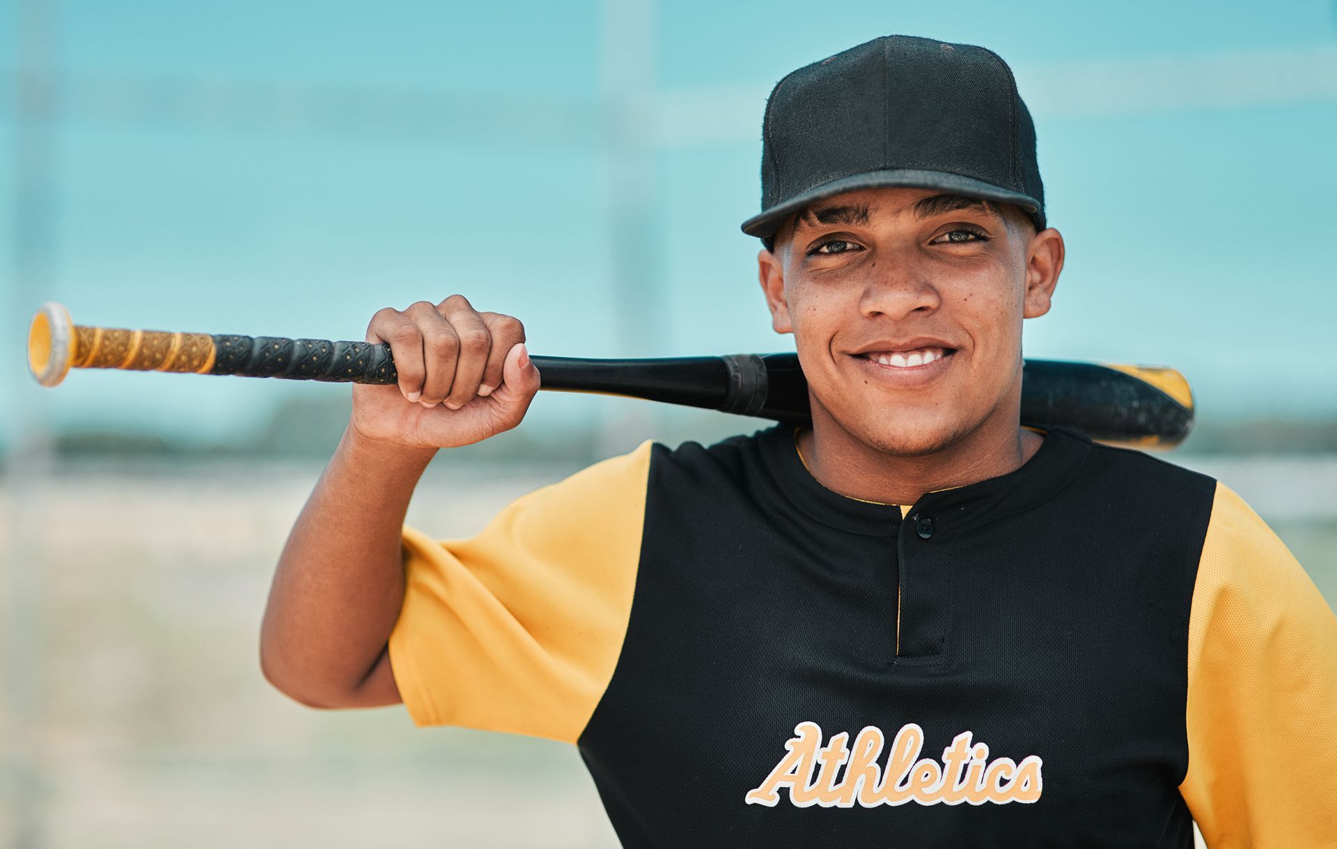 Baseball player in a black and yellow jersey holds bat, smiles.