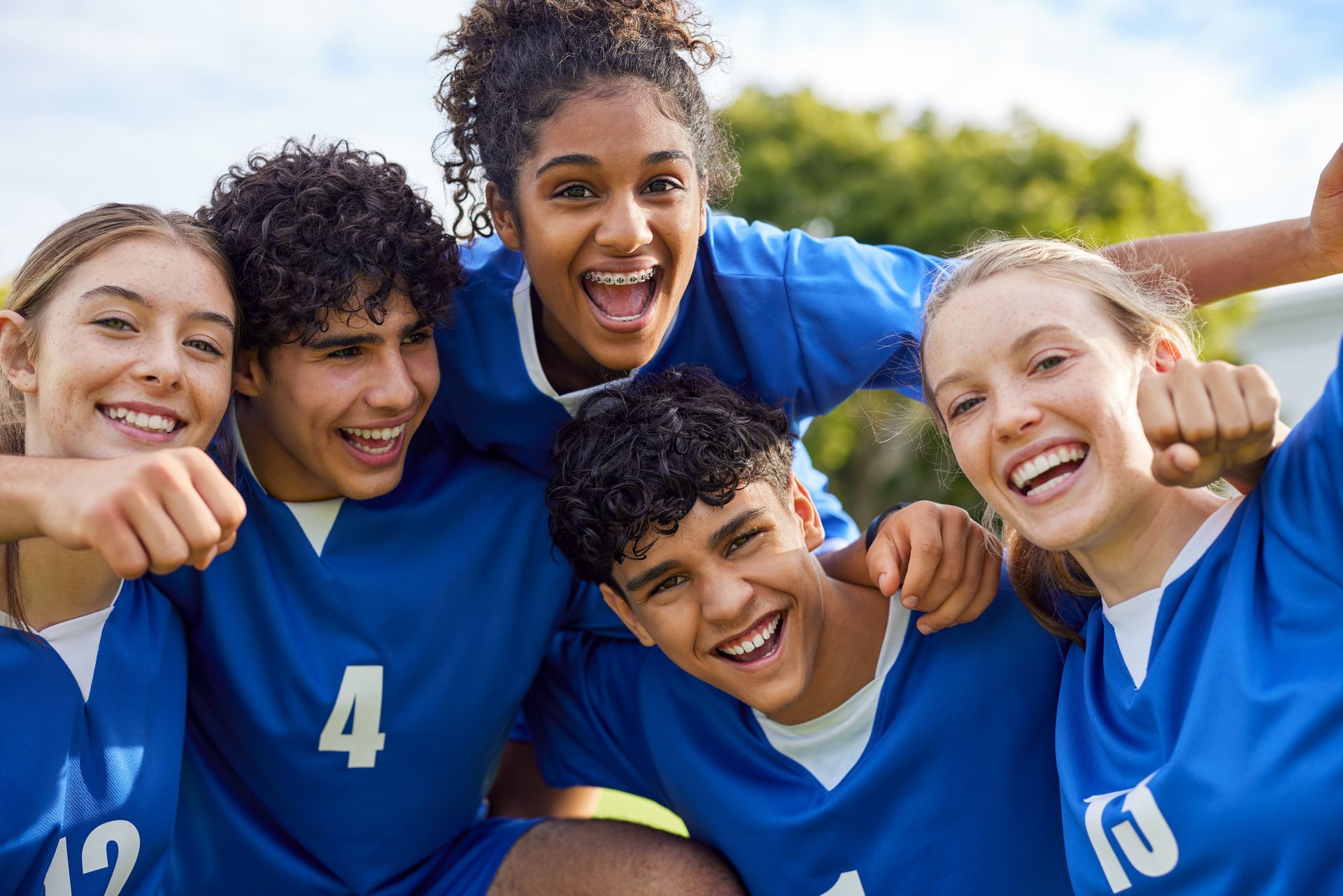 Five people in blue jerseys smiling and celebrating outdoors.