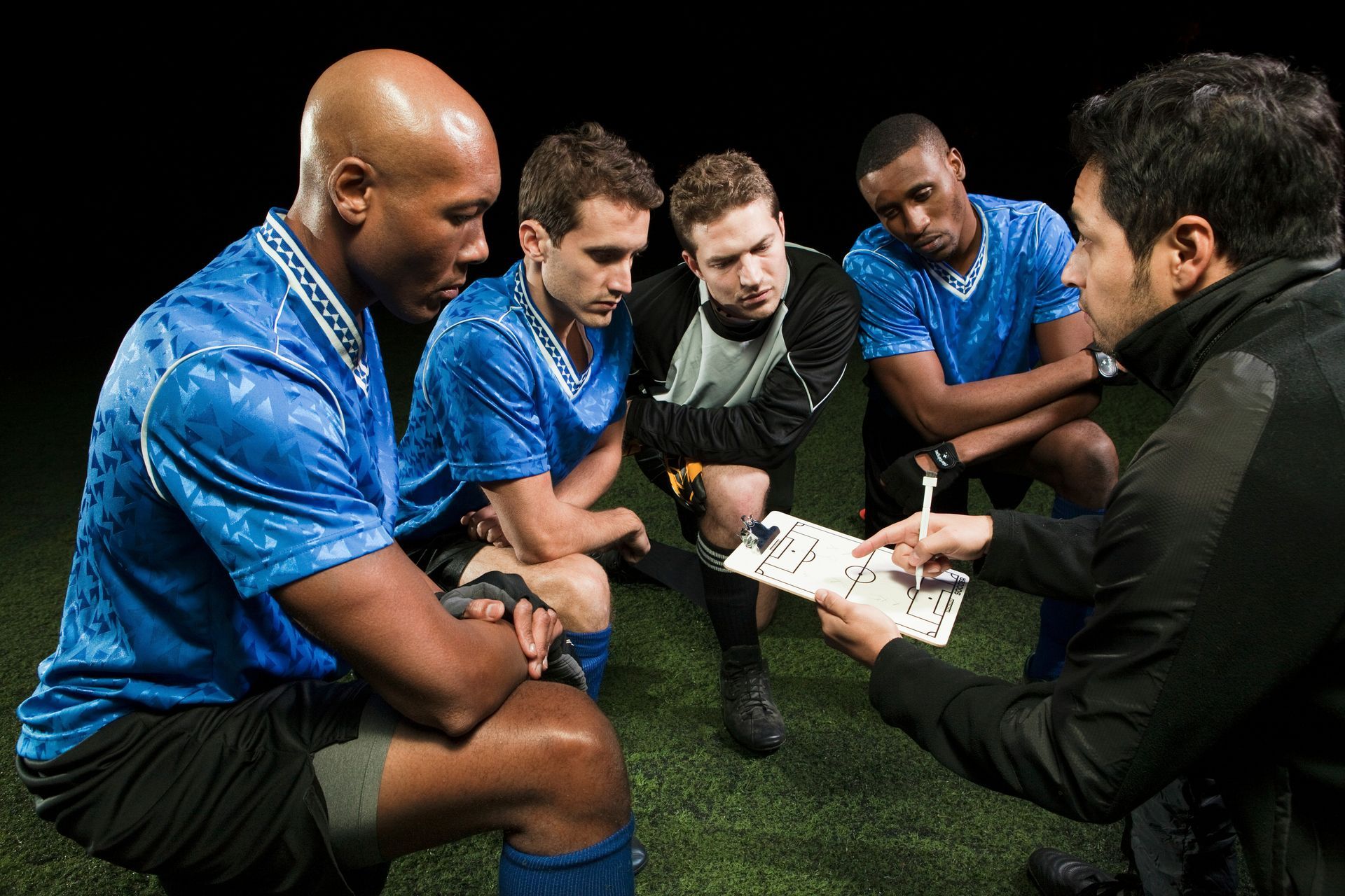 Soccer coach discussing strategy with four players on a field at night.