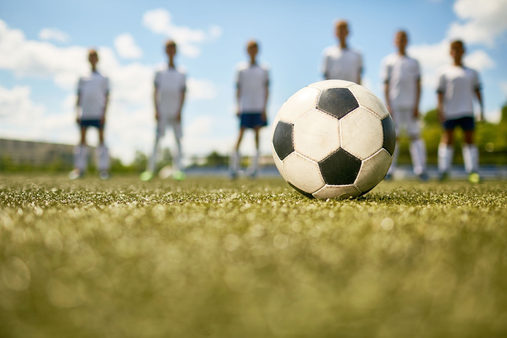 Soccer ball on green field, players in white uniforms in the background.