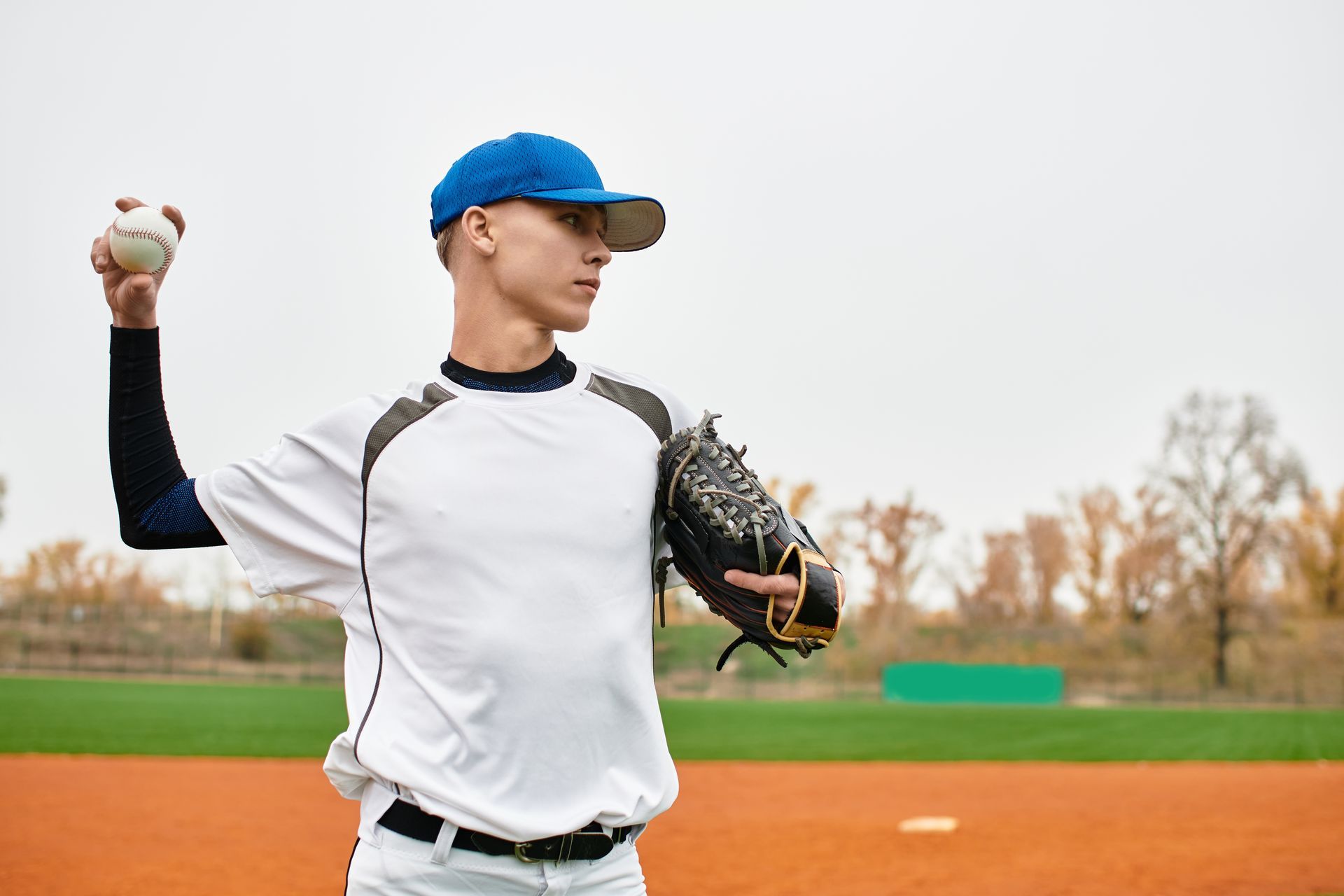 Baseball pitcher in a blue cap throws a ball on a red clay field.
