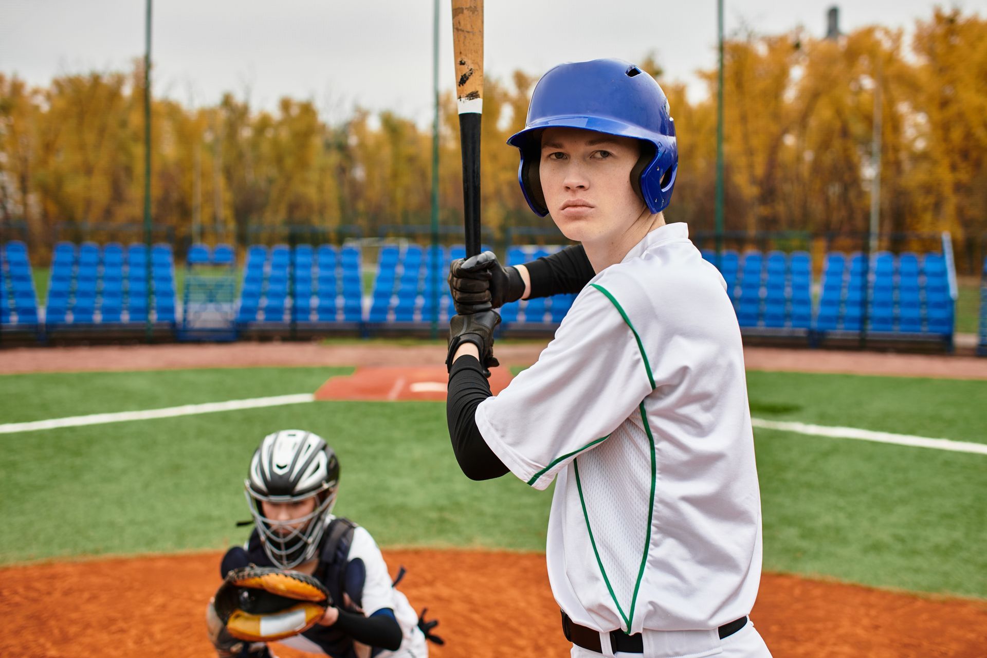 Baseball batter in blue helmet and white uniform, poised to hit. Catcher in gear behind him.