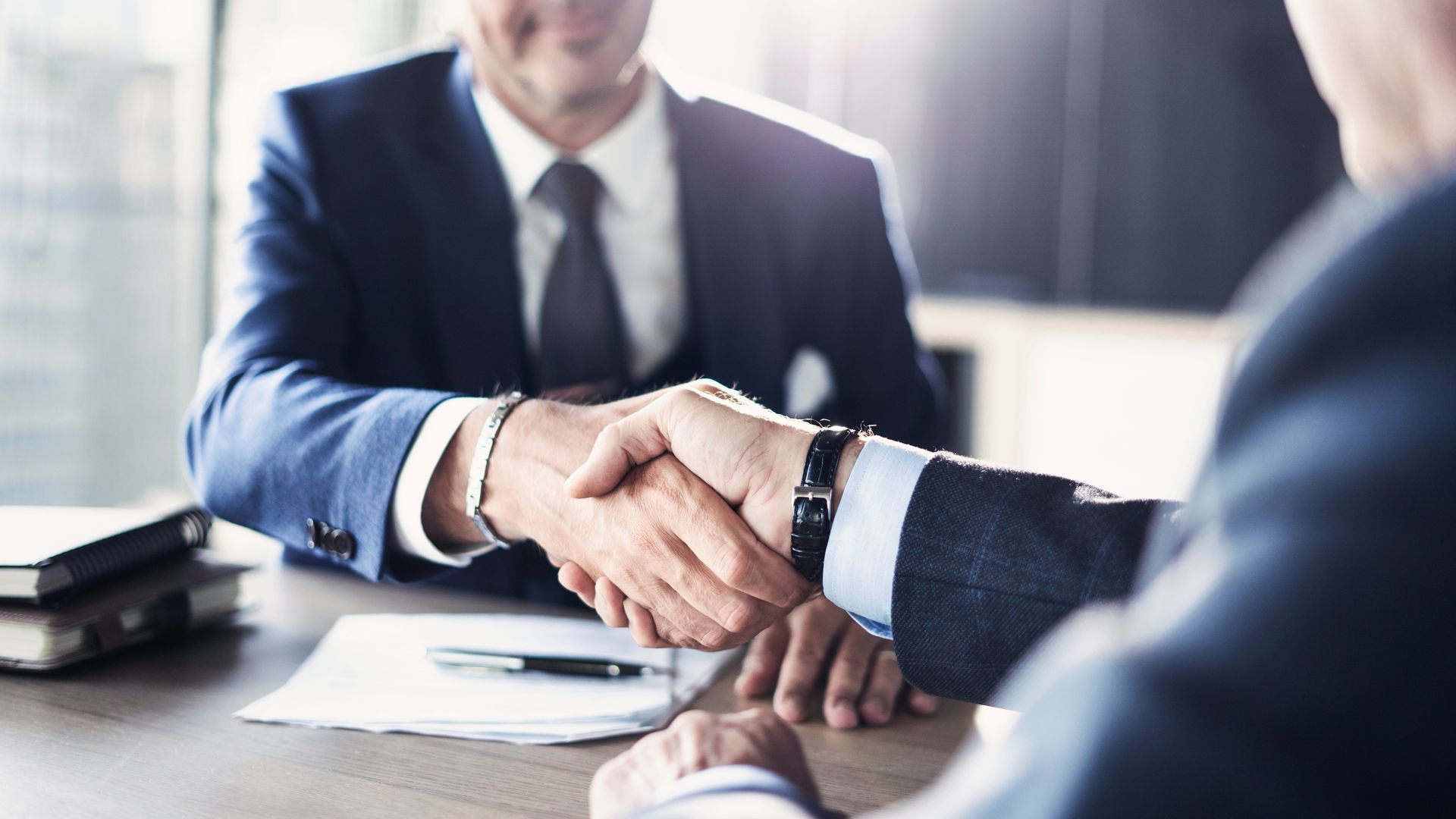 Two businesspeople shaking hands across a desk in a bright office