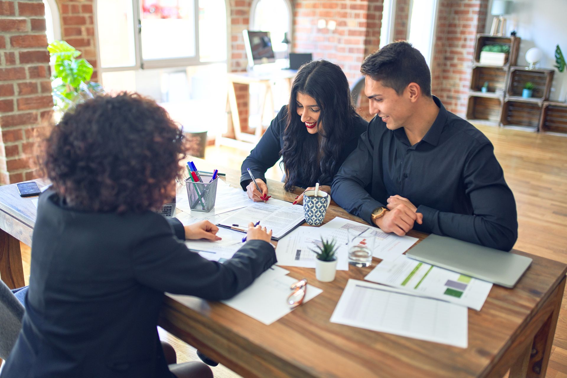 Three people reviewing documents at a desk in a bright office