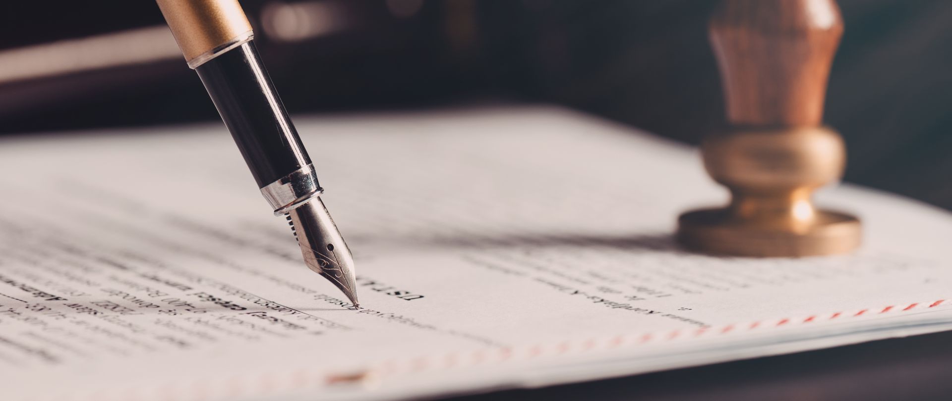 Close-up of a fountain pen signing a document beside a wooden stamp on a desk