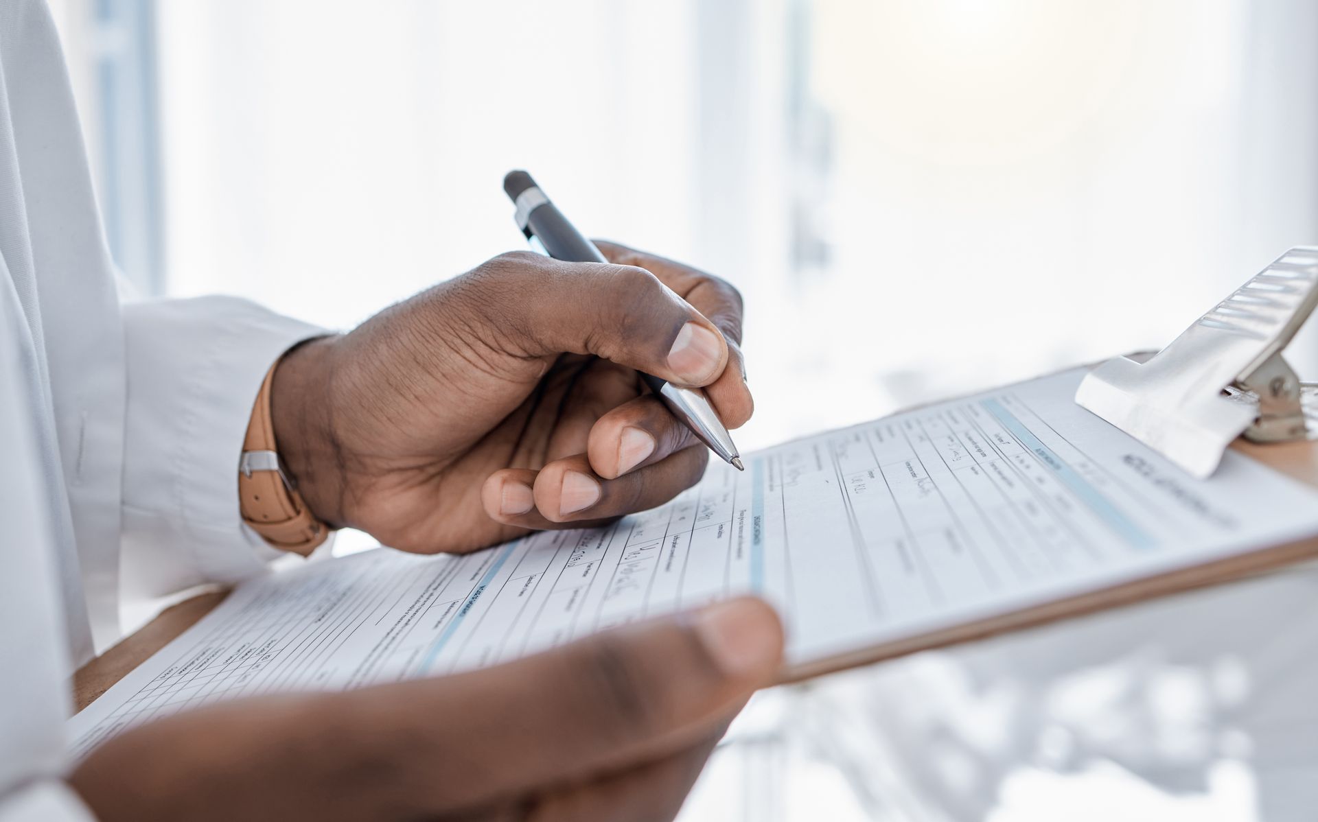 Hand holding a pen over a form on a clipboard in a bright office setting