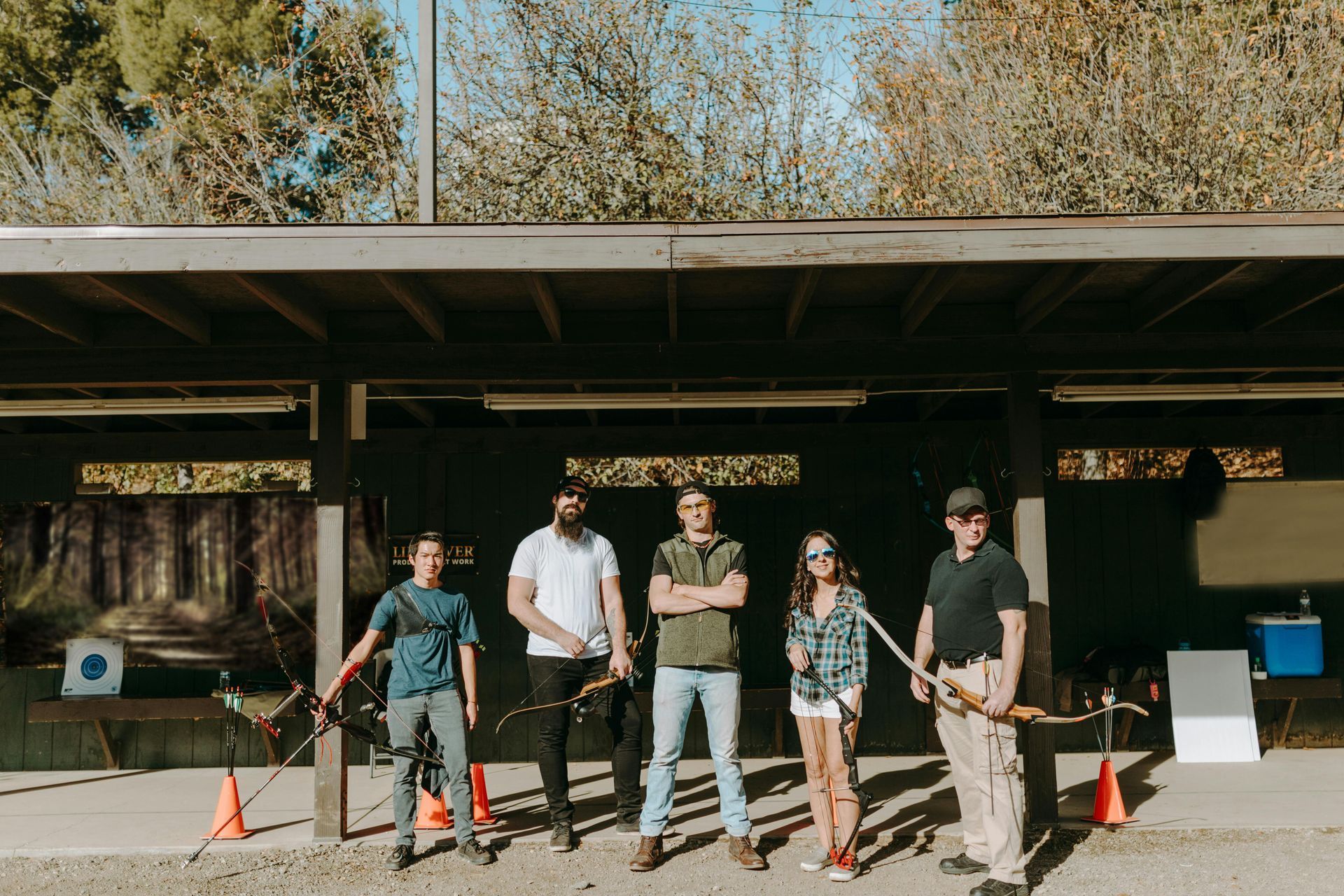 Six people with bows pose at an outdoor archery range.