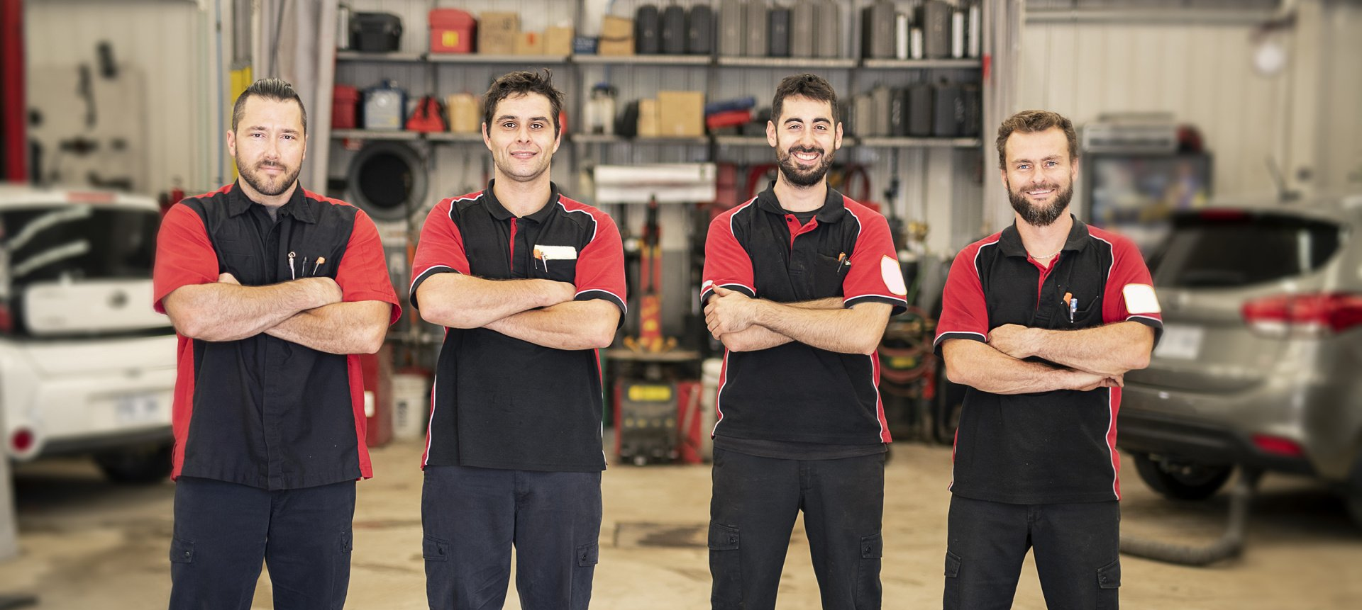 A group of mechanics are standing in a garage with their arms crossed.