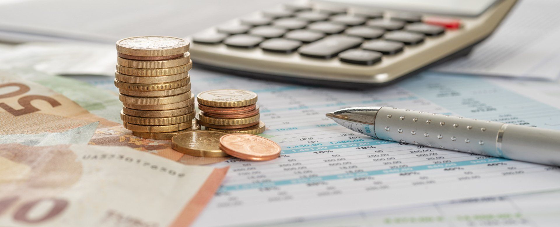 A stack of coins , a pen , and a calculator are on a table.