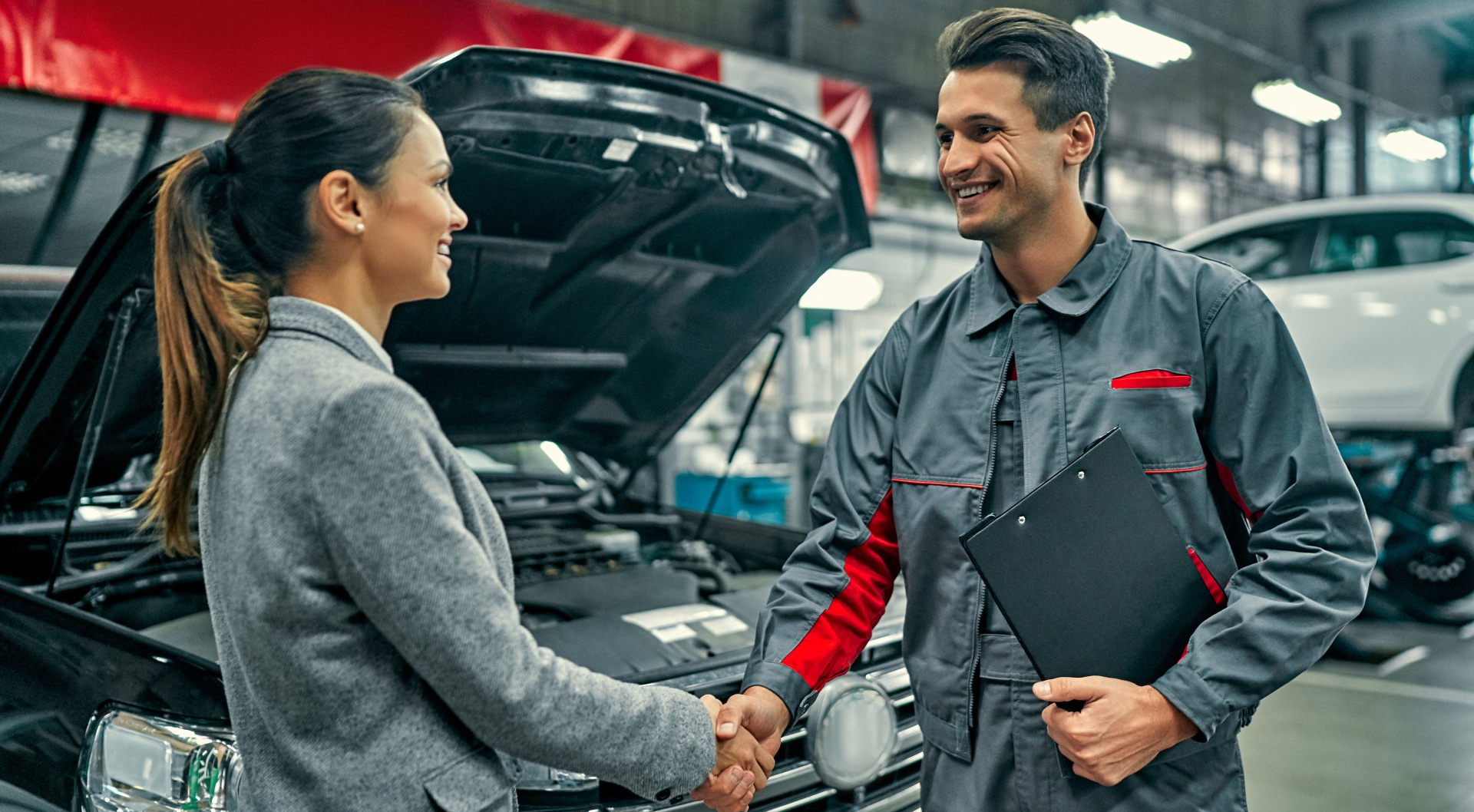 A woman is shaking hands with a mechanic in a garage.