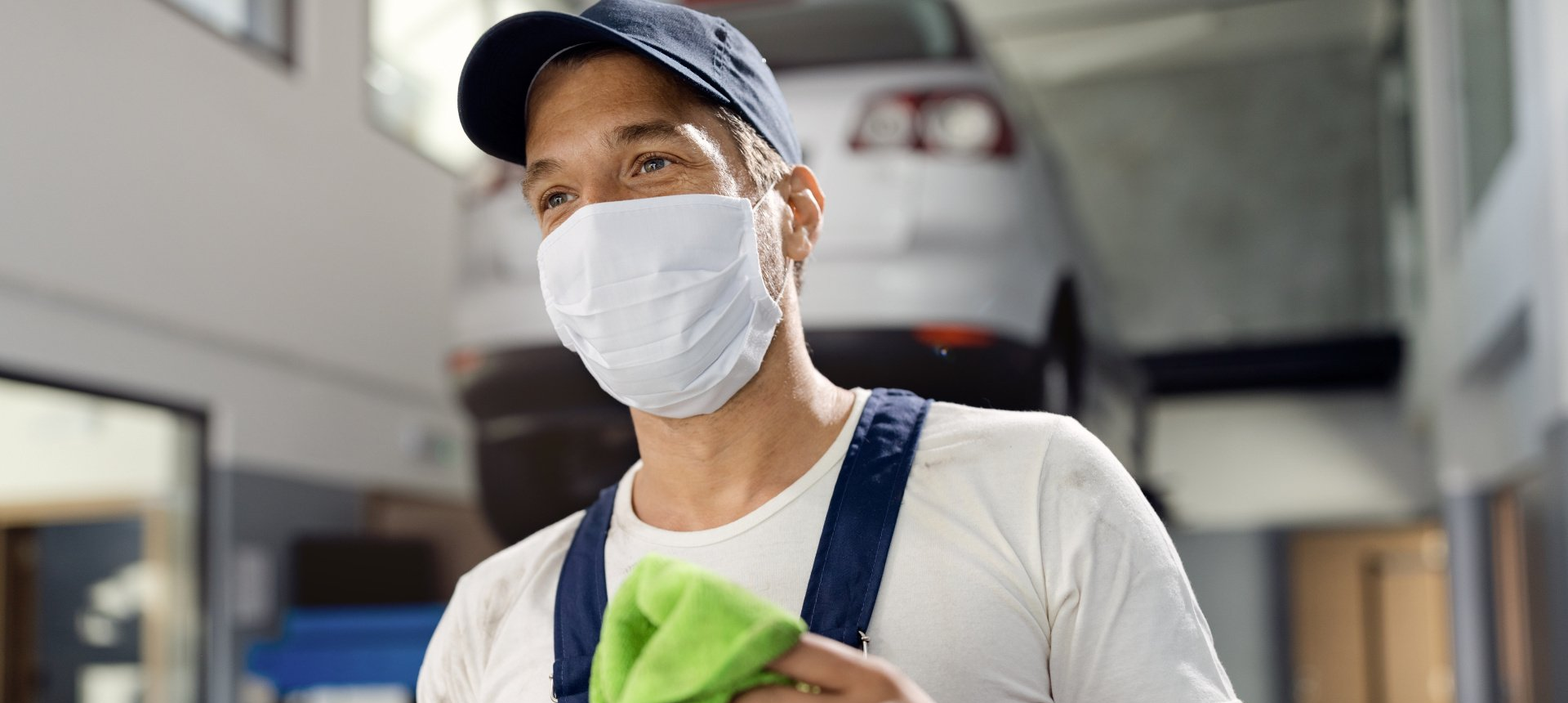 A man wearing a mask is cleaning a car in a garage.