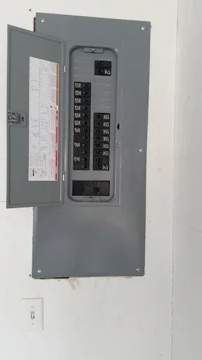 Open electrical breaker panel with gray metal door in a white wall