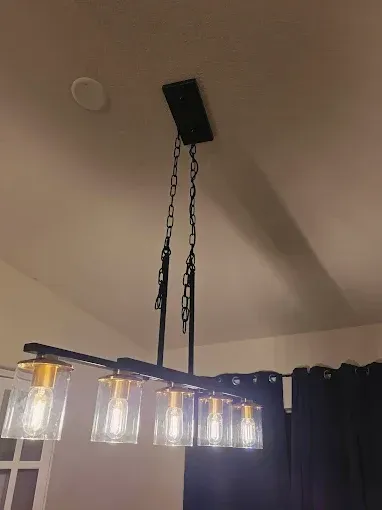 Black chandelier with glass shades hanging from the ceiling in a room with dark curtains.
