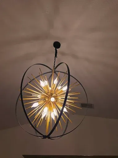 Modern pendant light with black wire frame and warm golden starburst bulb on a ceiling