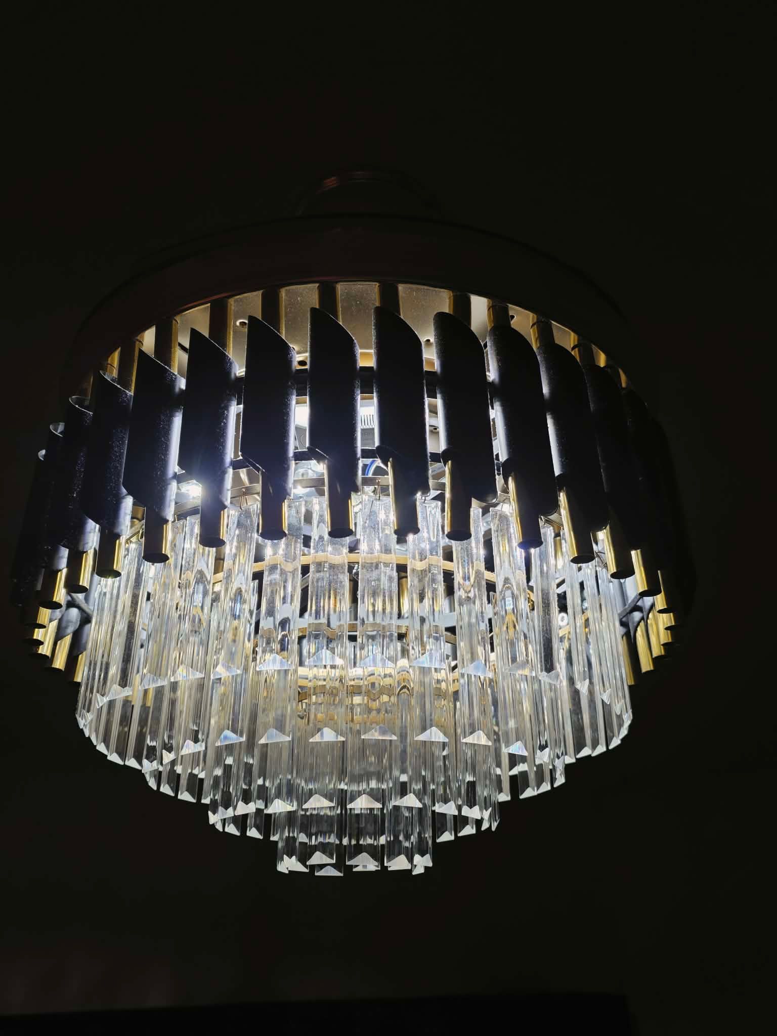 Crystal chandelier hanging from a dark ceiling, glowing with warm white lights.