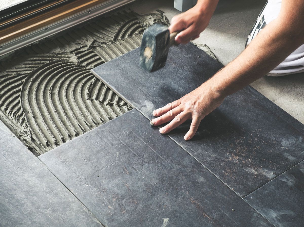 A person is laying a tile floor with a hammer.