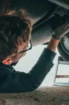 Mechanic working under a car, wearing gloves and glasses.