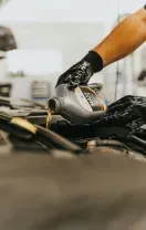 Hand pouring oil from a container into a car engine, in a mechanic shop setting.