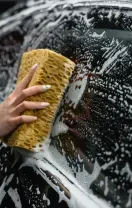 A person washes a black car with a soapy sponge.