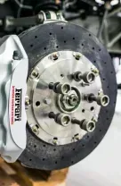 A close-up of a Ferrari brake disc and caliper, with the car's frame visible in a workshop setting.