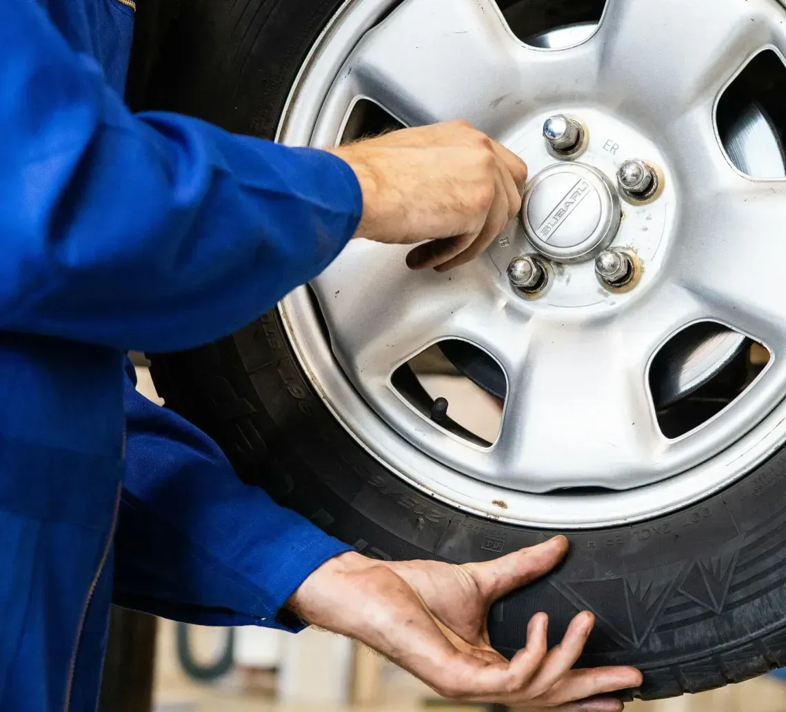Mechanic in blue jumpsuit removes lug nuts from a car tire in a garage.