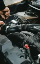 Hands of a mechanic working on a car engine, using a screwdriver.