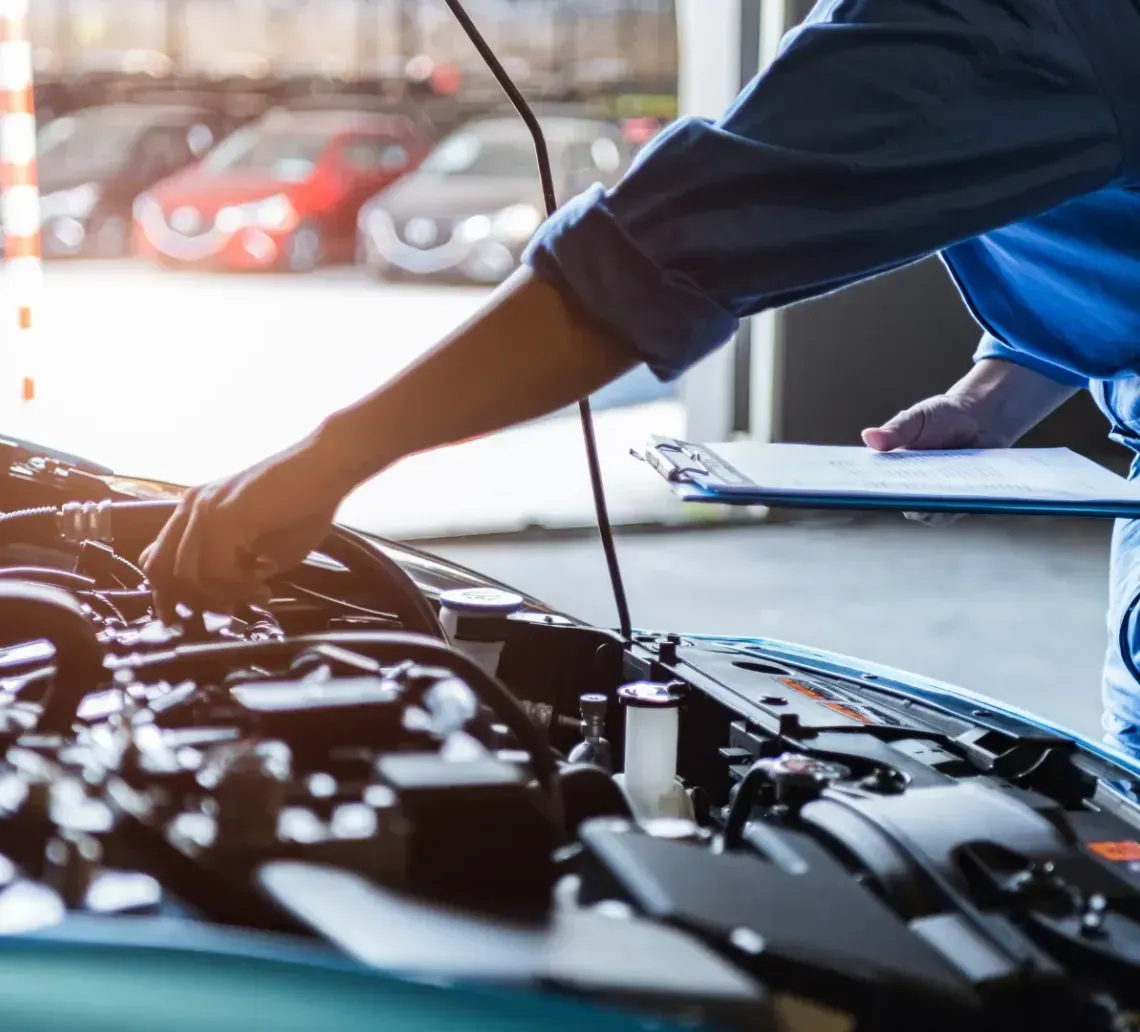Mechanic inspecting car engine with clipboard in an auto repair shop.