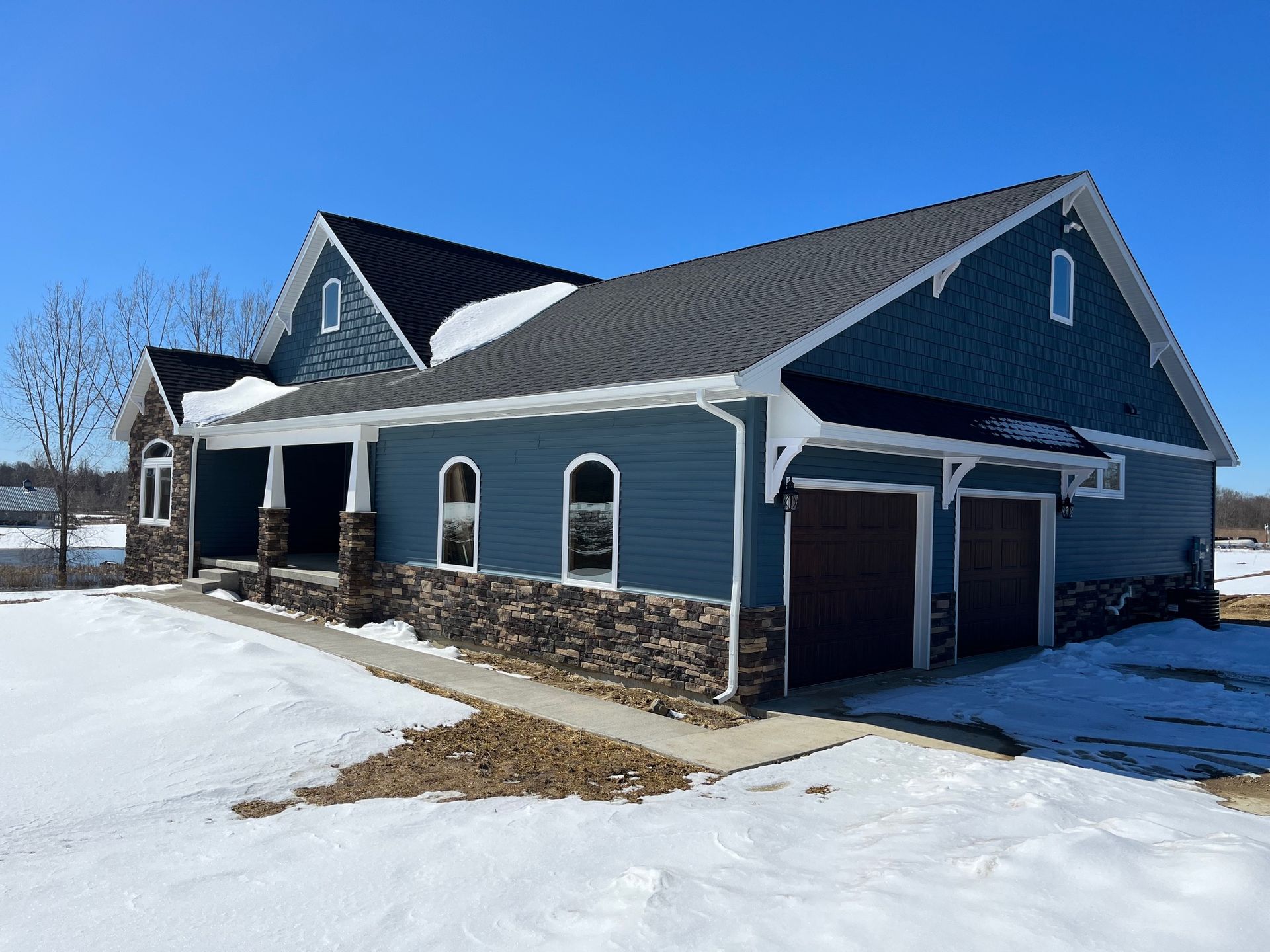 A blue house with a garage and a porch in the snow.