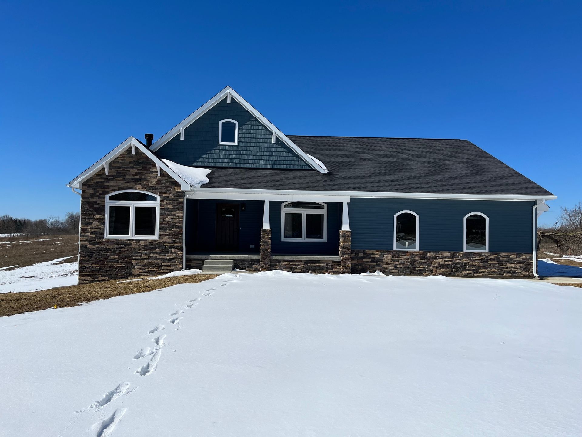 A blue house is sitting in the middle of a snowy field.