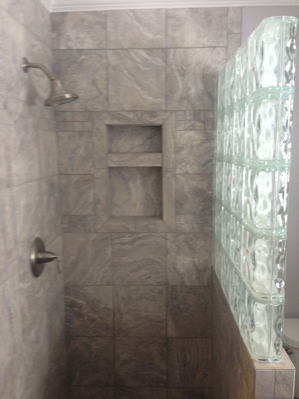 A shower with a glass block wall and a shower head.
