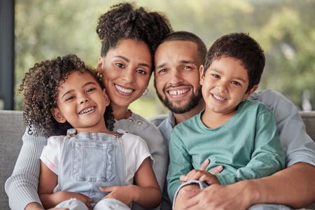 A family is sitting on a couch holding a drawing of their family.