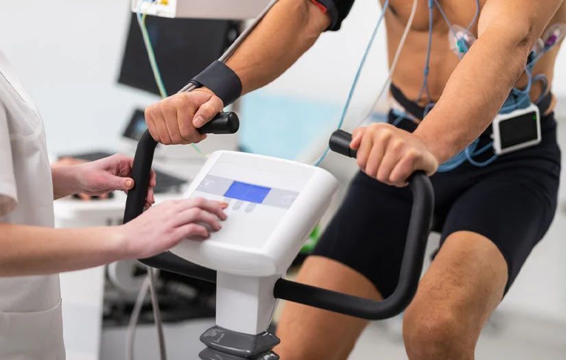 A man is riding an exercise bike while a nurse watches.