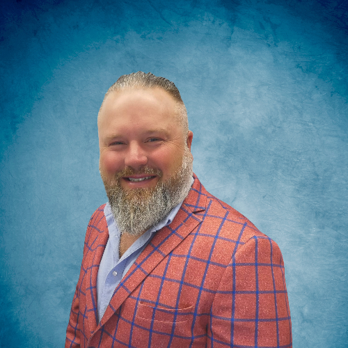 A man with a beard is wearing a red and blue plaid jacket.