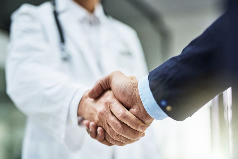 A doctor and a businessman are shaking hands in a hospital.