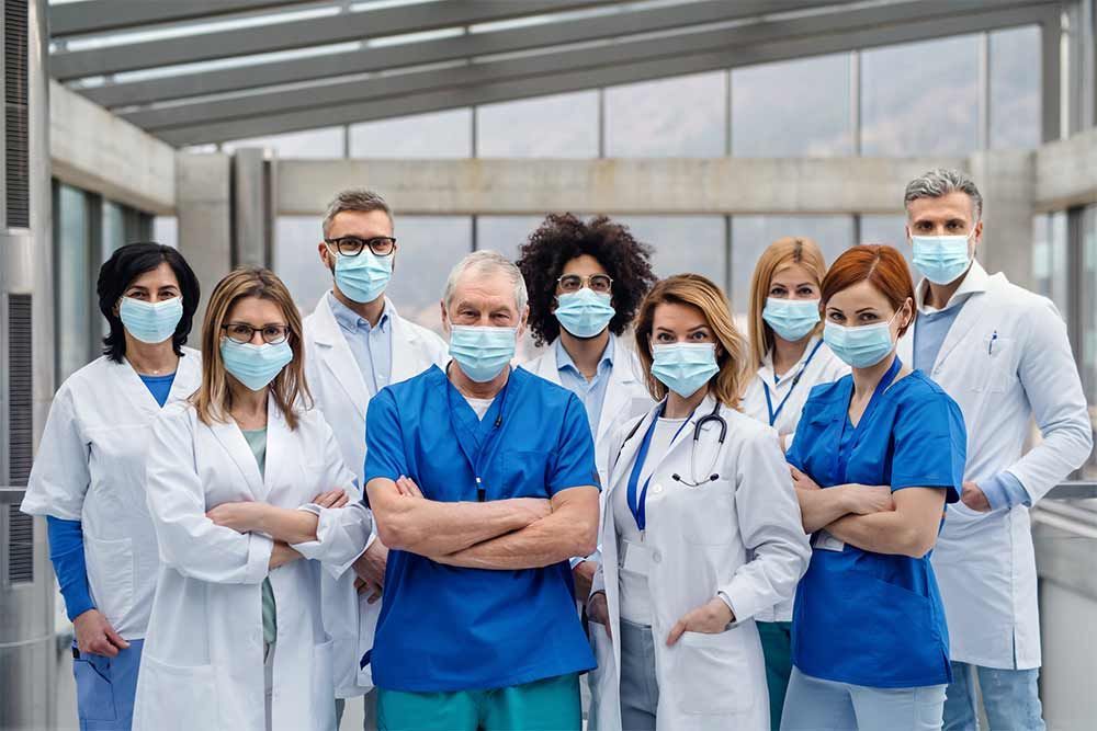 A group of doctors and nurses wearing face masks are posing for a picture.