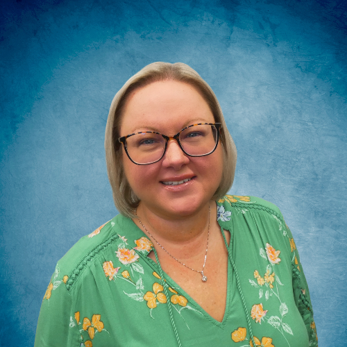A woman wearing glasses and a green floral shirt is smiling for the camera.