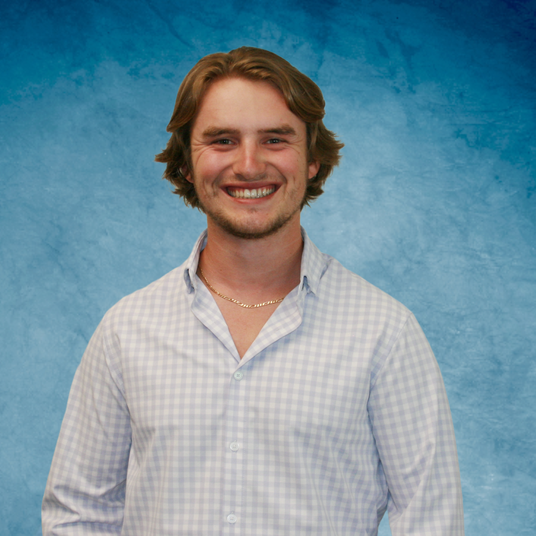 A man with a beard and a blue shirt is standing in front of a blue background.