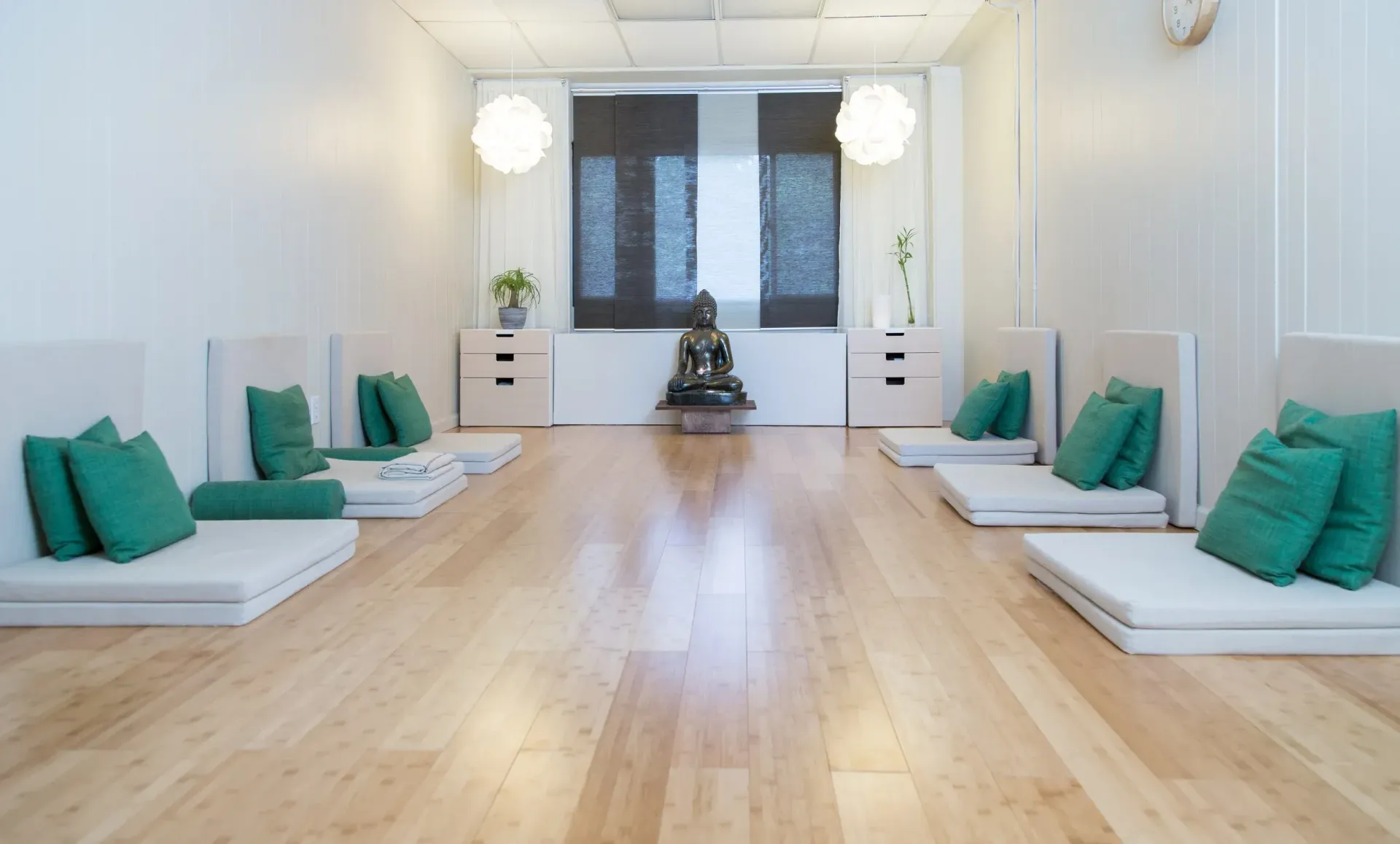 Yoga studio with cushioned floor seating and green pillows, wooden floor, statue centered.