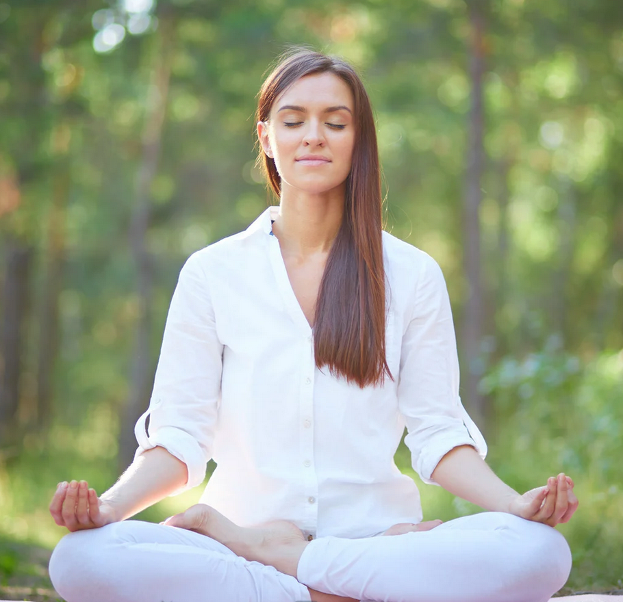 Woman seated, eyes closed, hand on chest, meditating indoors near a lamp.