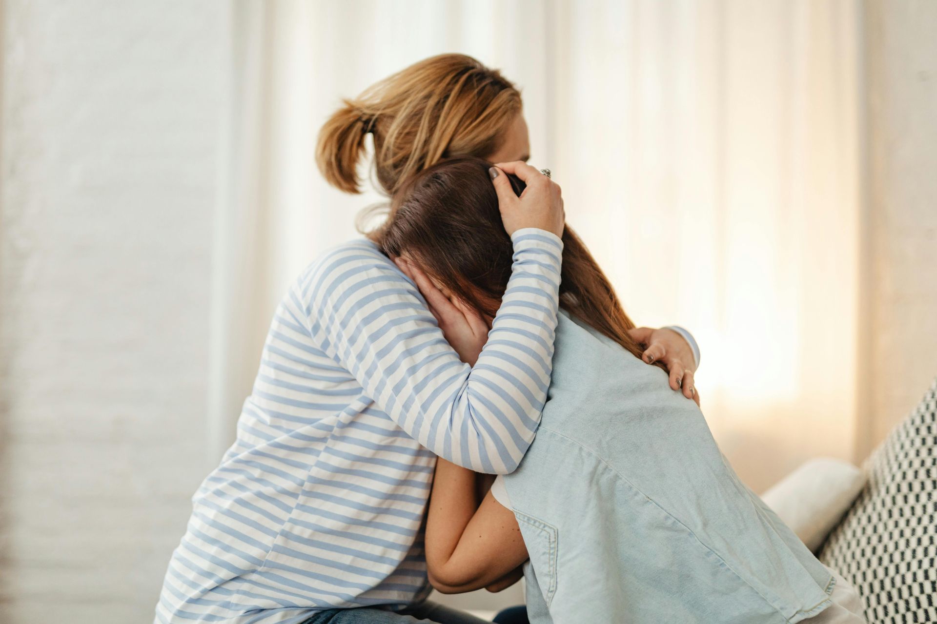 Woman and child embracing indoors, child appears to be crying.