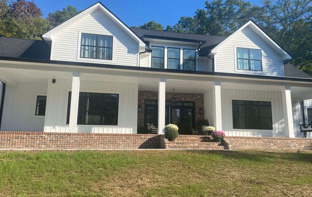 White two-story house with columns, brick steps, and a front porch on a grassy slope