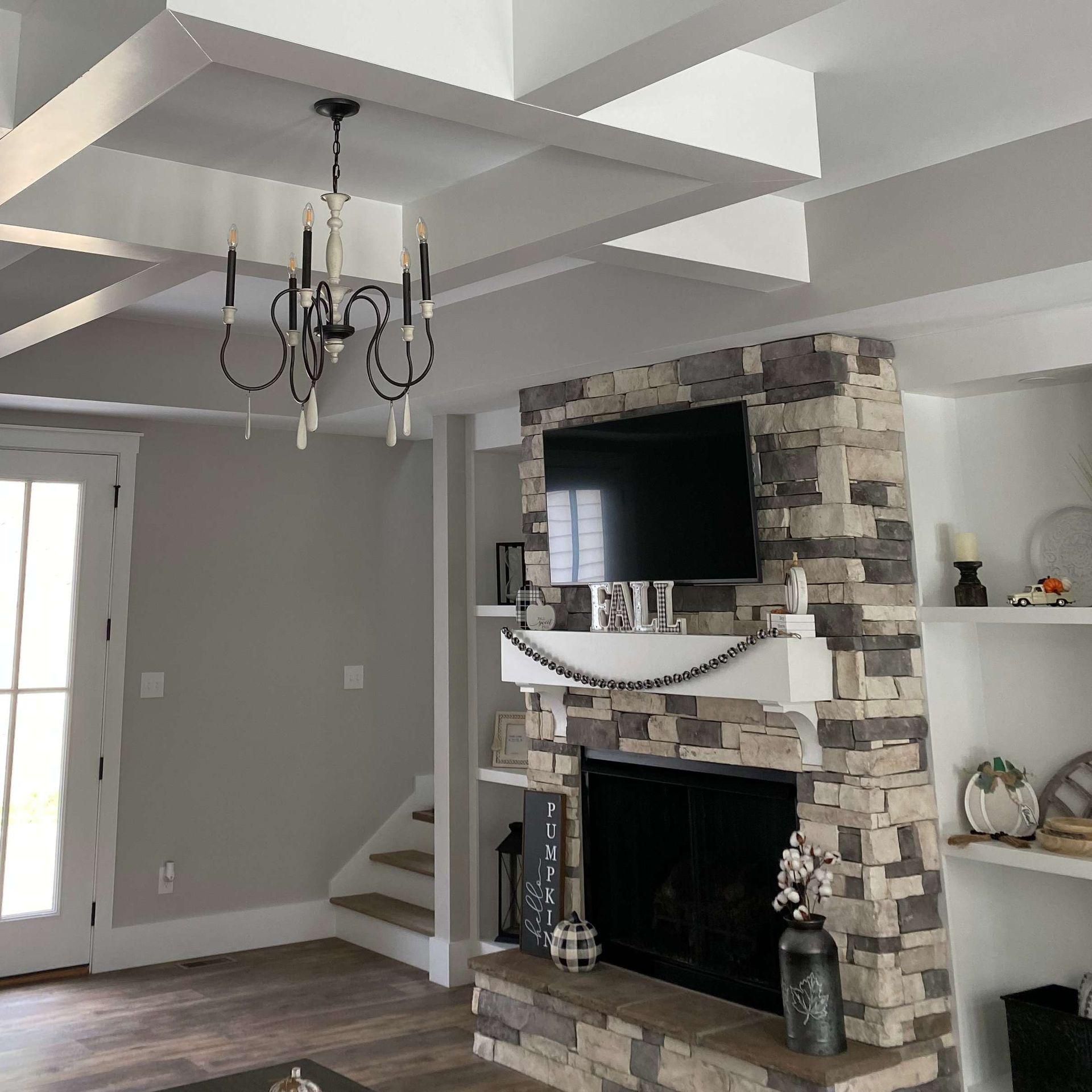 Bright living room with exposed beams, stone fireplace, chandelier, and hardwood floors