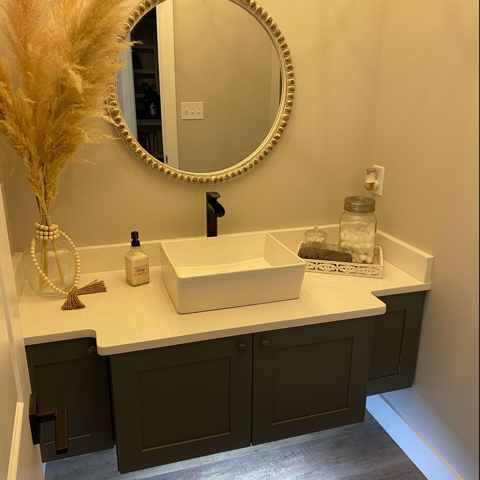 Modern bathroom vanity with round mirror, white countertop, dark cabinets, and pampas grass decor
