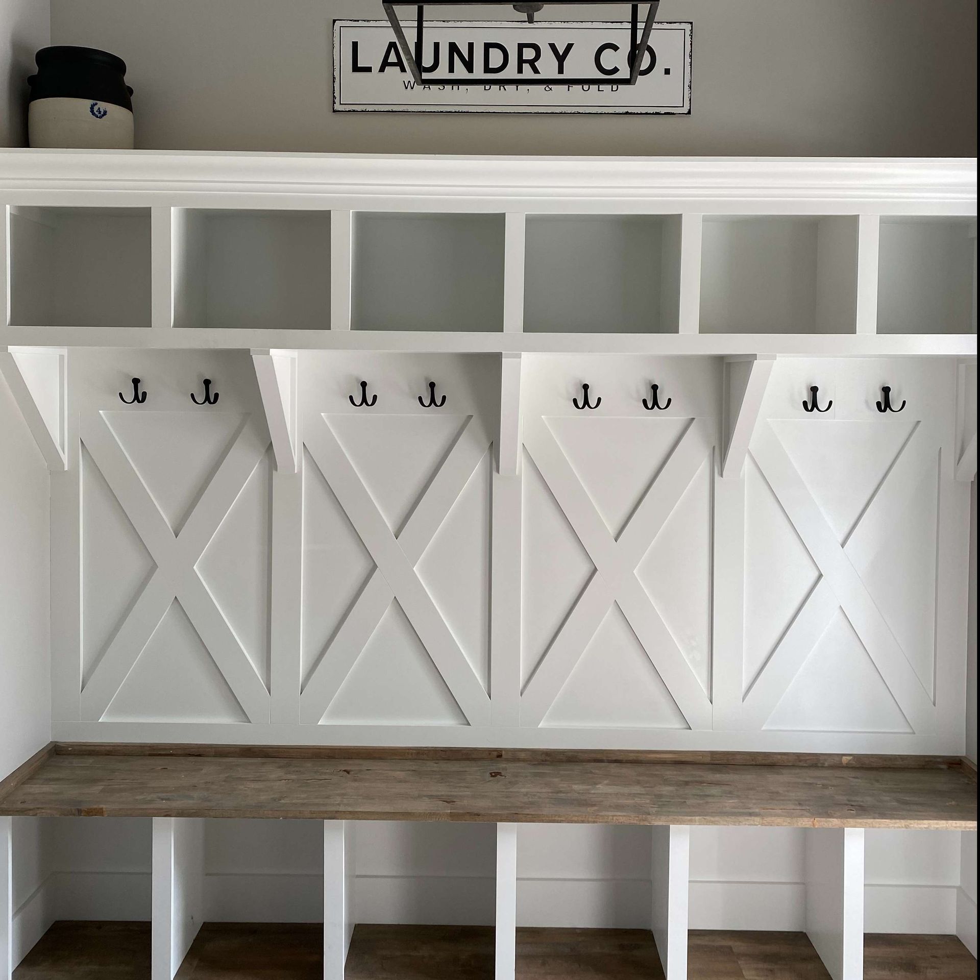 White laundry room cubbies and hooks with a wooden bench and “Laundry Co.” sign above