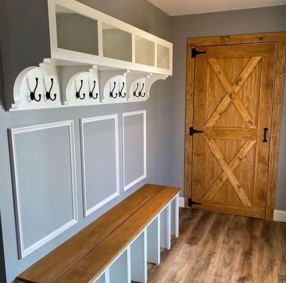 Mudroom bench with hooks and cubbies beside a wooden barn door in a gray entryway.