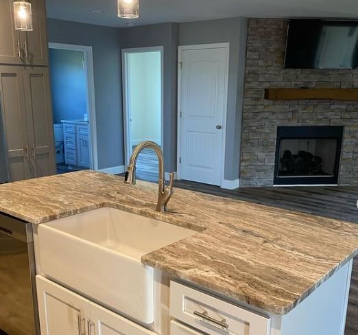 Modern kitchen with island sink, granite countertop, stainless fridge, and stone fireplace in the background