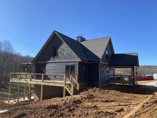 Dark gray house under construction with a wooden ramp and deck on a bare dirt lot