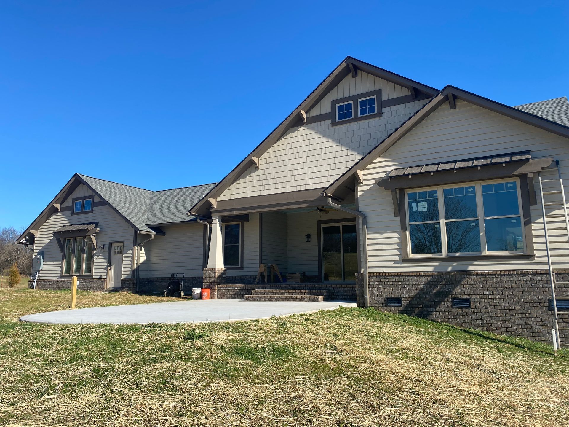 Modern house exterior with stone accents, large windows, and a sloped lawn under a clear blue sky