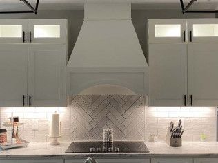 Modern kitchen with gray cabinets, white countertops, and a central stove under a large range hood.